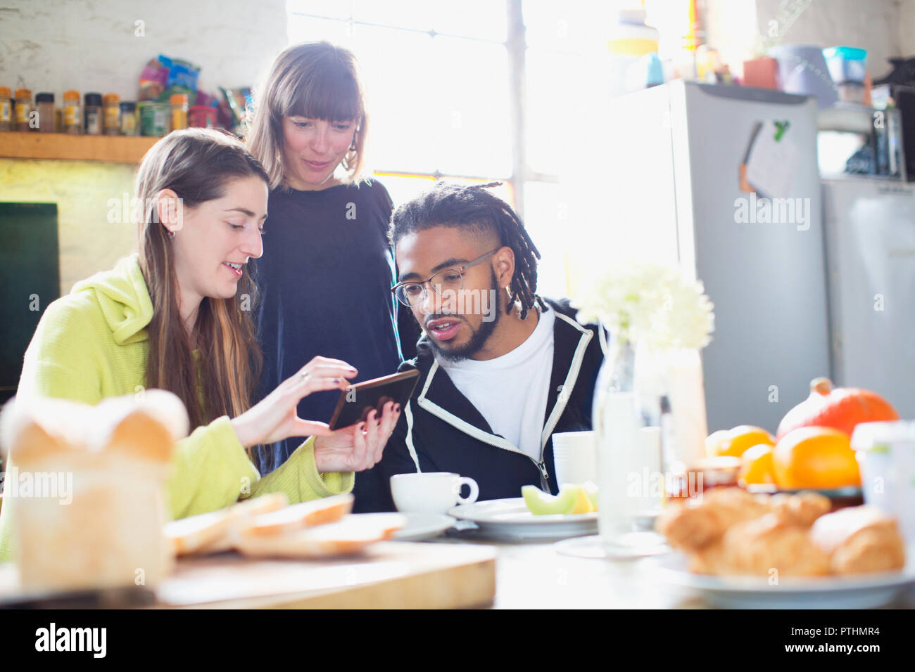 I giovani adulti universitario amici utilizzando smart phone al tavolo per la colazione in appartamento Foto Stock