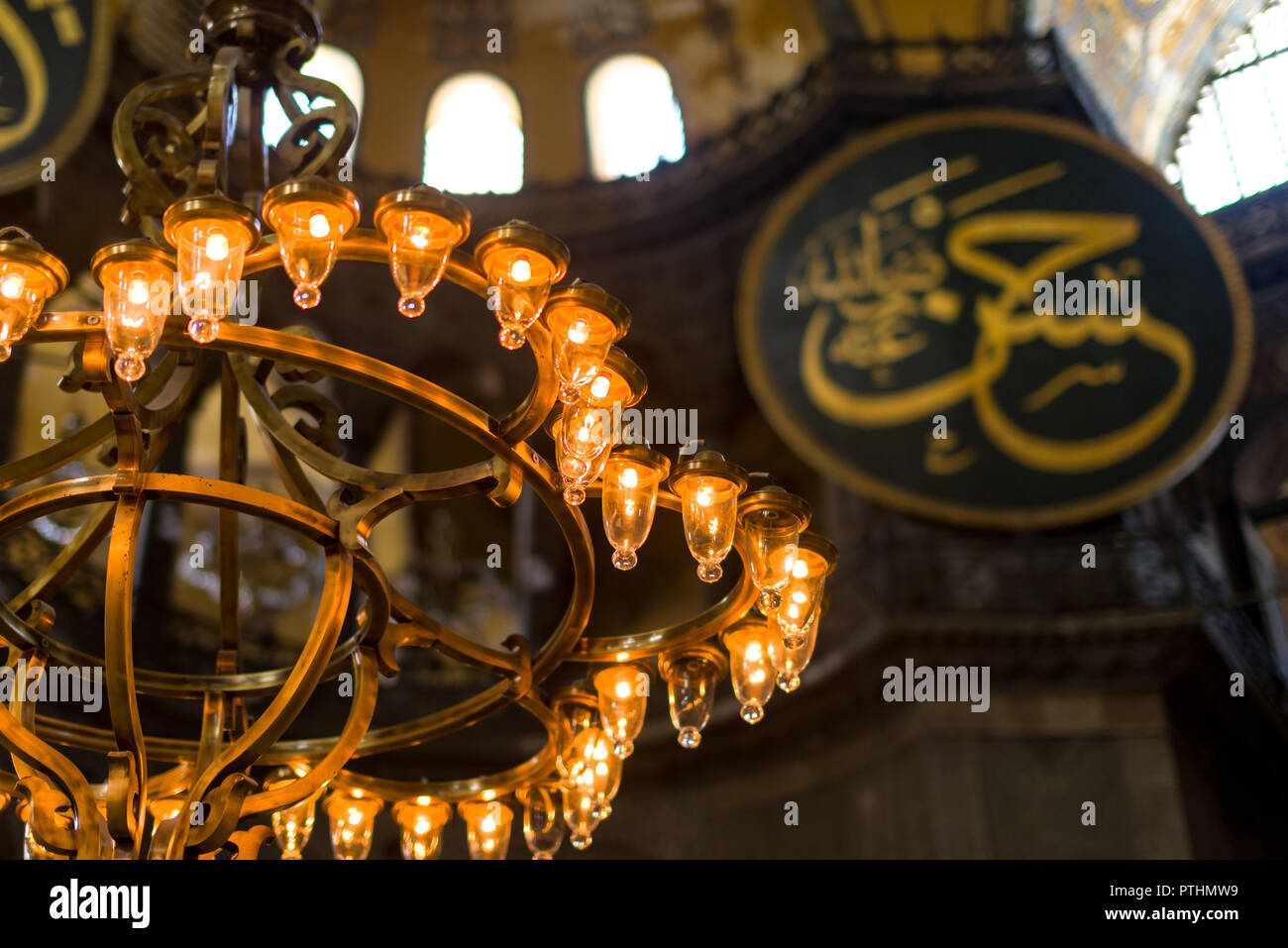 Vista su dei lampadari che illuminano la navata principale interno del Museo Hagia Sophia con cupola e roundel calligrafico in background, Istanb Foto Stock