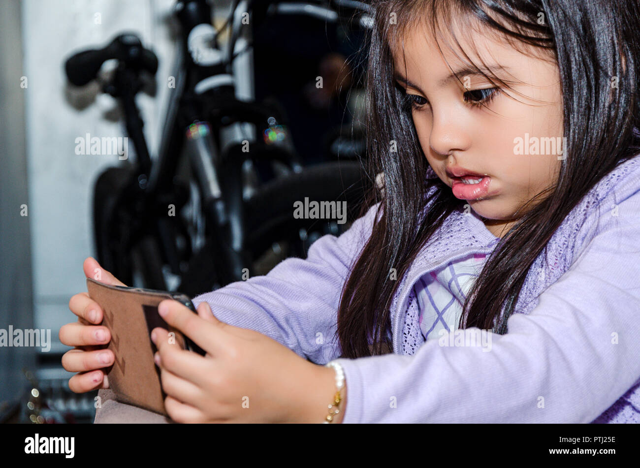 Incantevole piccola ragazza seduta sul lettino usando un moderno smartphone Foto Stock