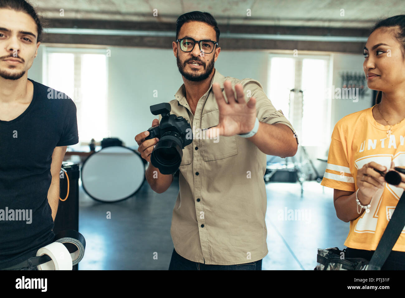 Fotografo guidare un modello circa la posa durante un servizio fotografico. Fotografo con i suoi assistenti facendo scattare una foto in studio. Foto Stock