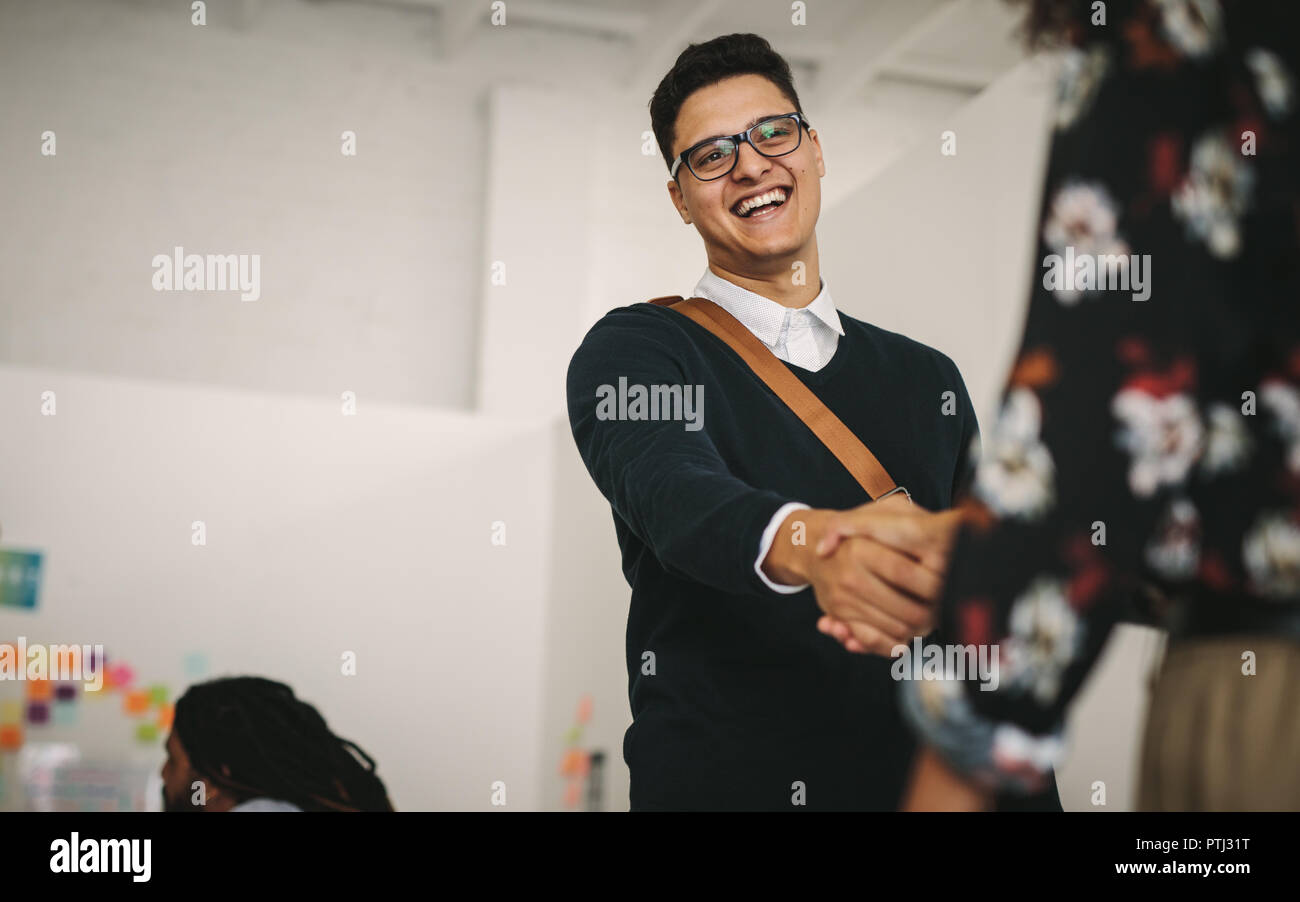 Imprenditore e il messaggio di saluto parlando a un cliente in ufficio. Imprenditore sorridente stringe la mano con un collega. Foto Stock