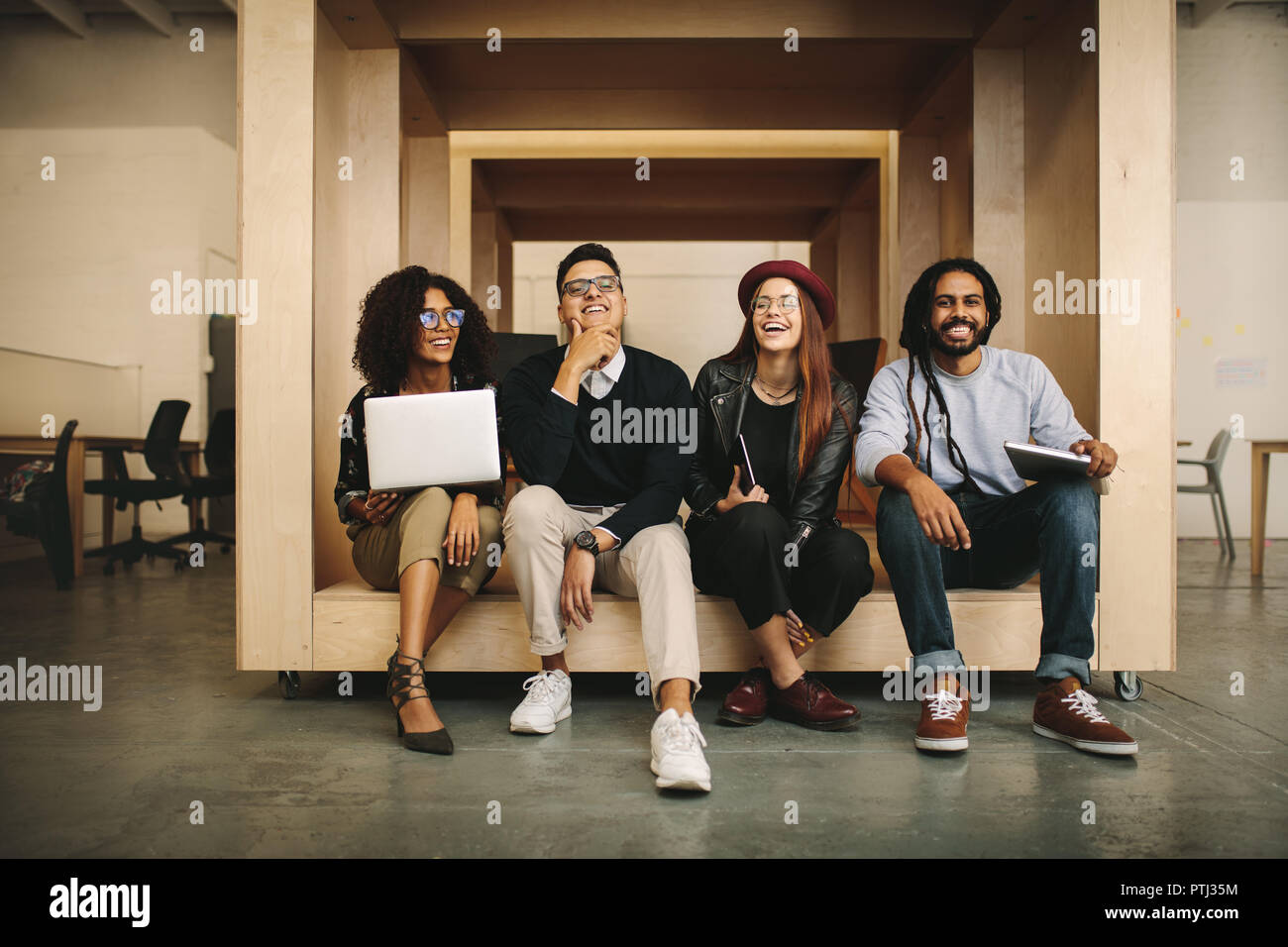 colleghi d'affari seduti in un recinto quadrato in ufficio che si rilassano. Partner aziendali sorridenti seduti in ufficio con laptop insieme. Foto Stock