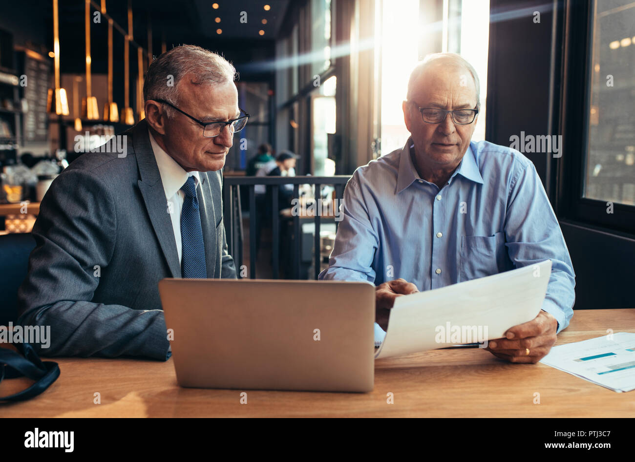 Gli imprenditori Senior discutendo su una relazione durante la riunione in una caffetteria. Due imprenditori maturi che lavorano in cafe con computer portatile sul tavolo e guardando un docu Foto Stock
