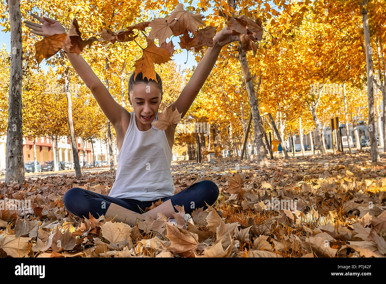 Ragazza seduta in un parco giocando con foglie Foto Stock