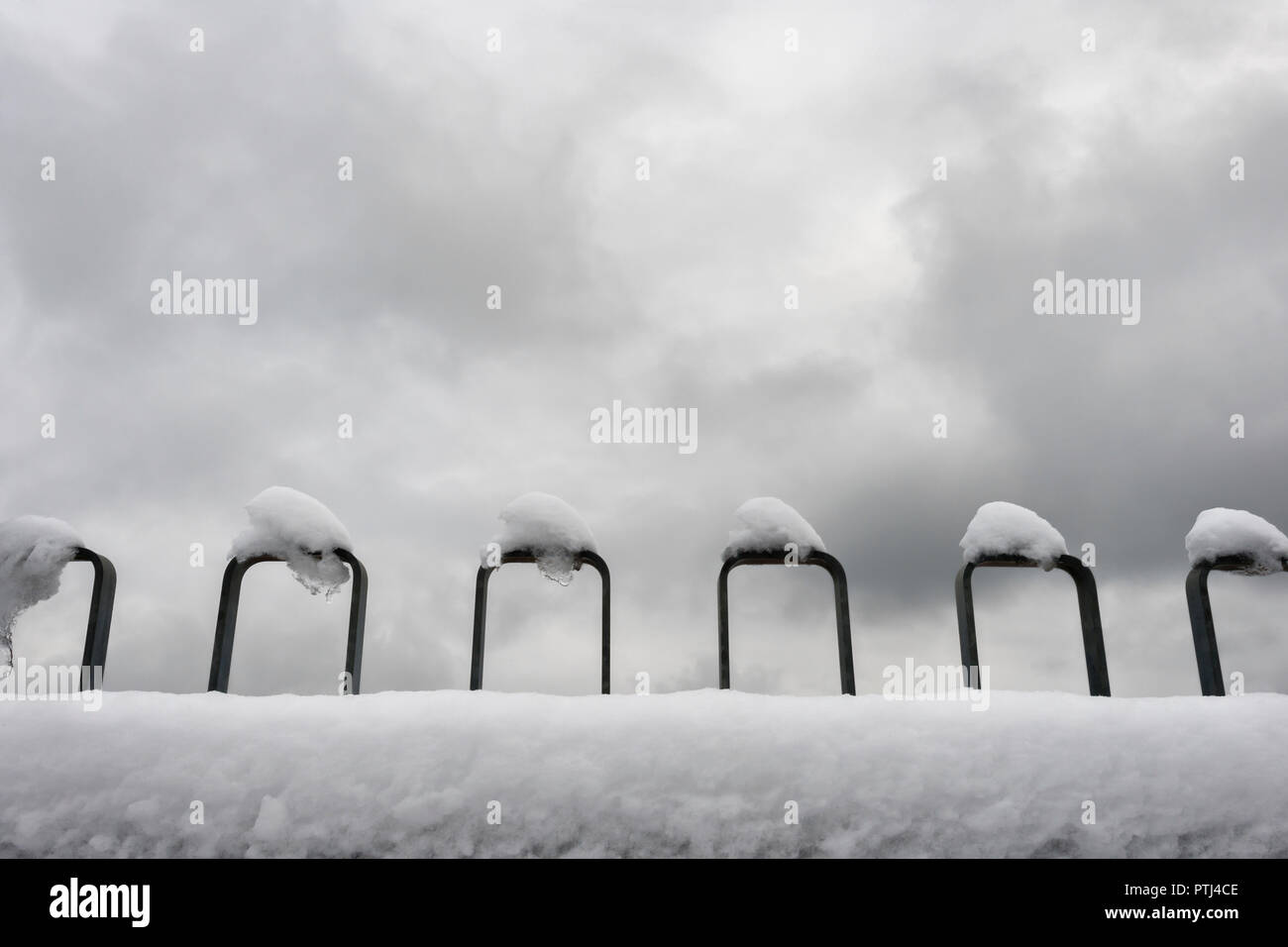 Una concezione minimalista della coperta di neve della ringhiera contro un cielo nuvoloso. Foto Stock