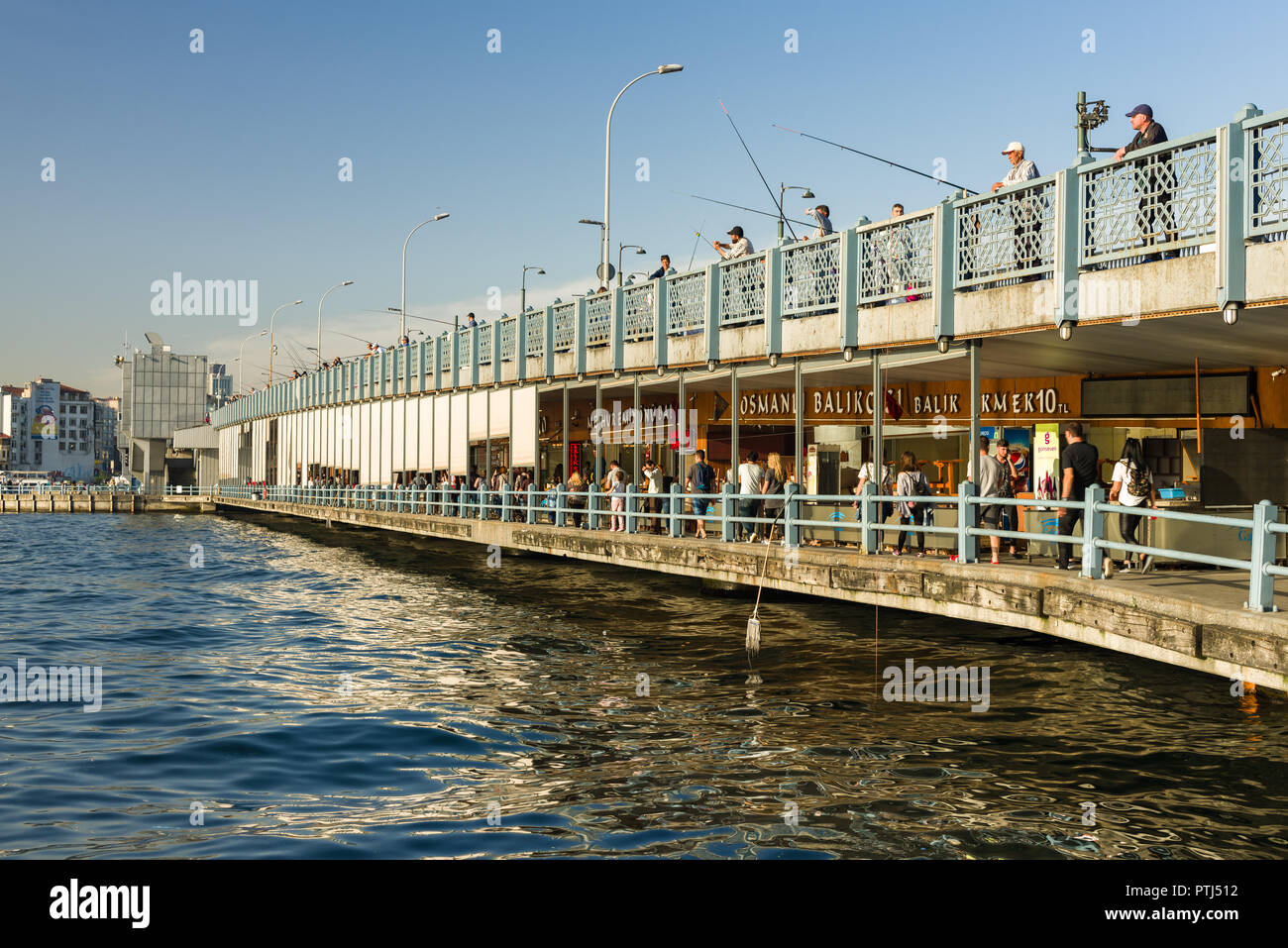 Il Ponte di Galata con pescatori pesca nonché le persone a piedi ristoranti passato sotto il Bosforo in primavera la luce del pomeriggio, Istanbul, Turchia Foto Stock