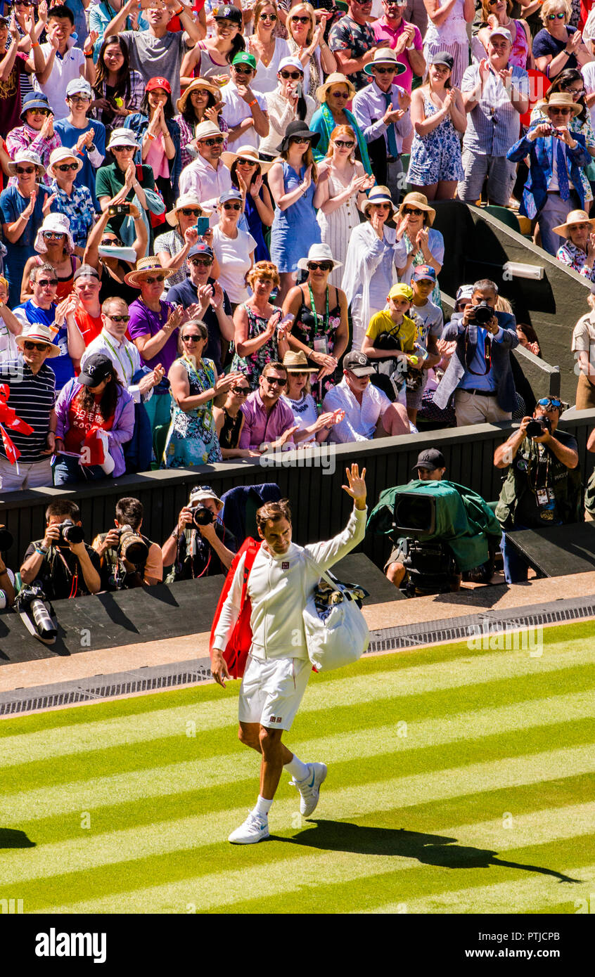 Roger Federer le onde a la folla in corte centrale dopo aver vinto il suo primo match il primo giorno dei campionati di Wimbledon. Foto Stock