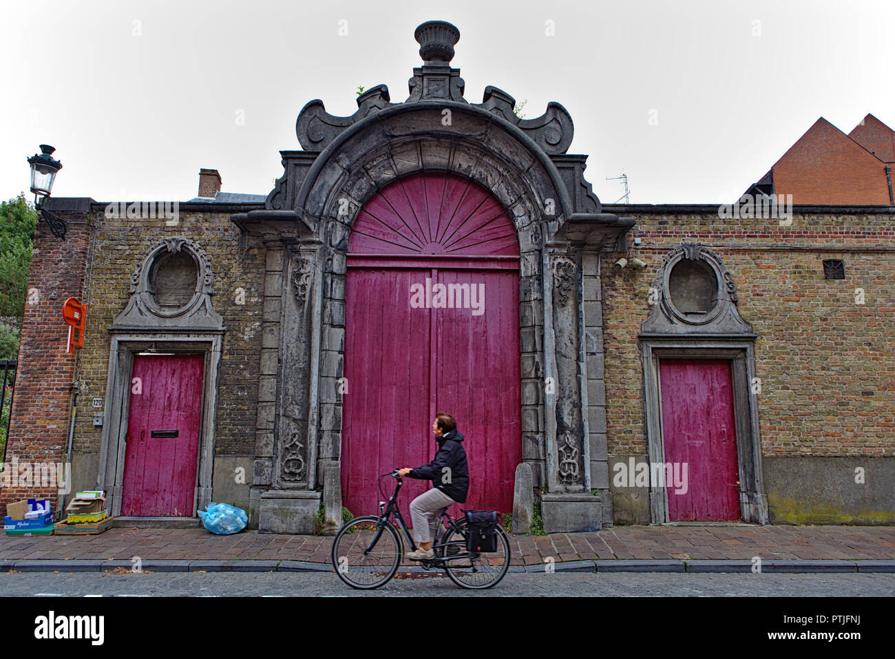 Uomo in bicicletta nella parte anteriore del vecchio porta rosa in Bruges Foto Stock