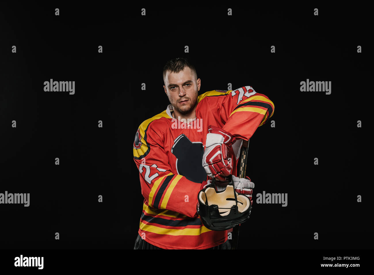 Bel giocatore professionale del hockey di ghiaccio in piedi con attrezzature sportive e guardando la telecamera isolato su nero Foto Stock