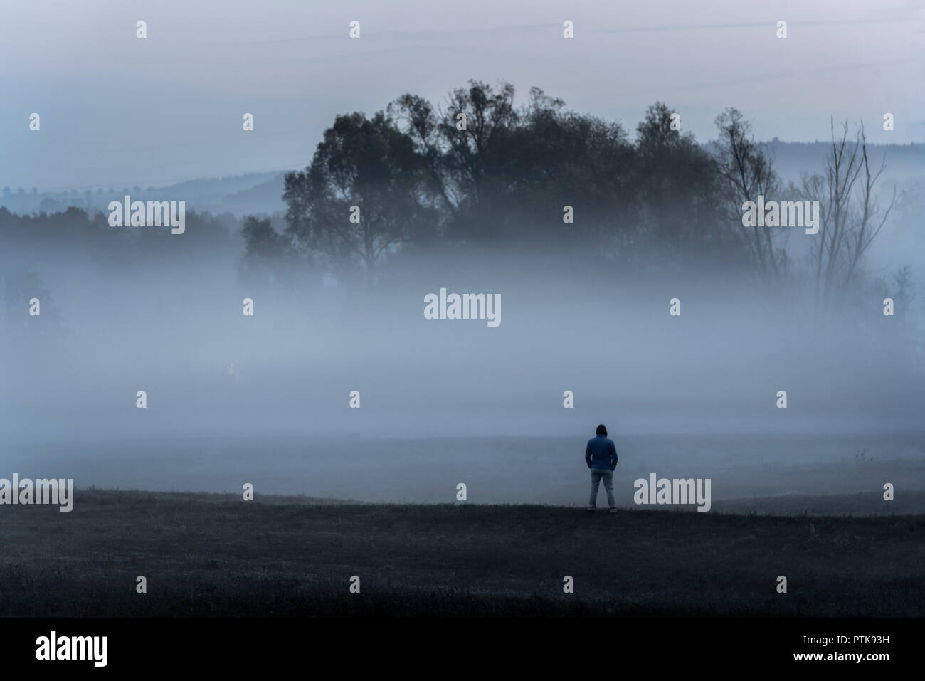 Carattere drammatico paesaggio con un uomo in piedi da solo nel freddo, su di un prato, contemplando la fitta nebbia, vicino Schwabisch Hall, Germania. Foto Stock