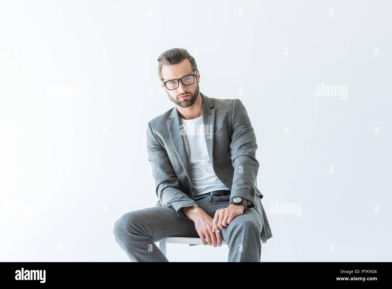 Imprenditore elegante in abito grigio seduto su una sedia, isolato su bianco Foto Stock