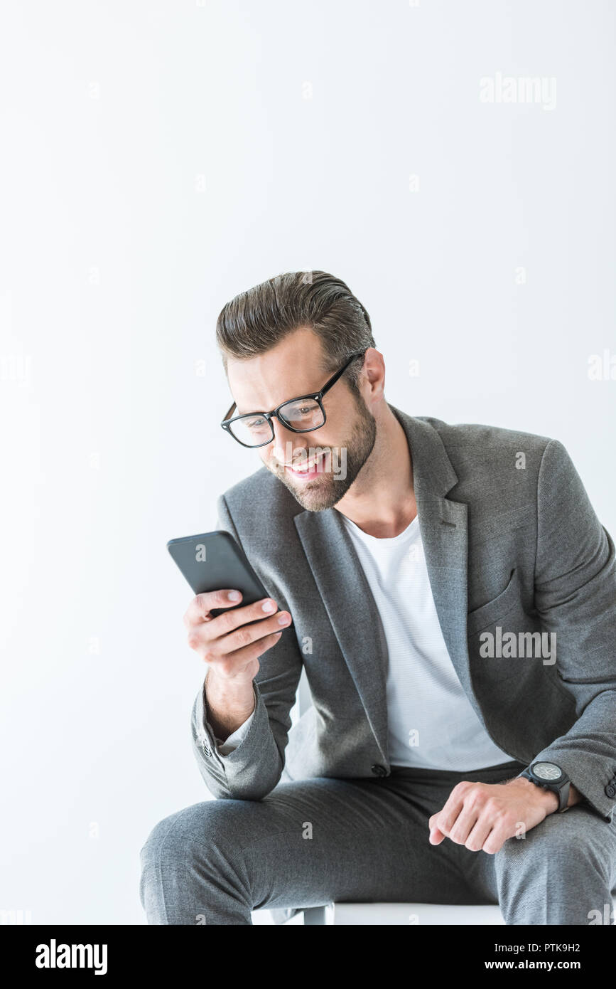 Elegante uomo in abito grigio utilizzando lo smartphone, isolato su bianco Foto Stock
