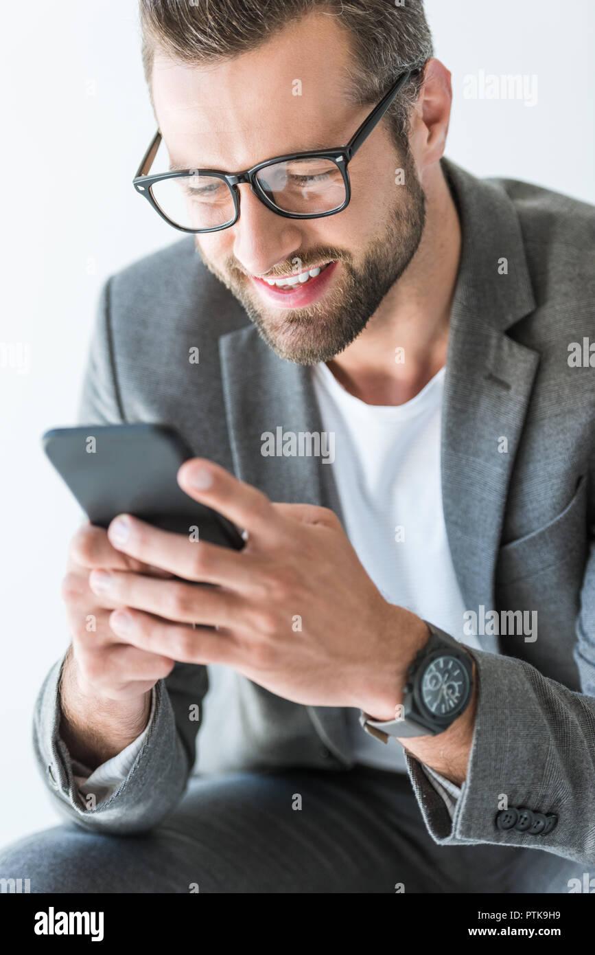Felice l'uomo barbuto in giacca grigia utilizza lo smartphone, isolato su bianco Foto Stock