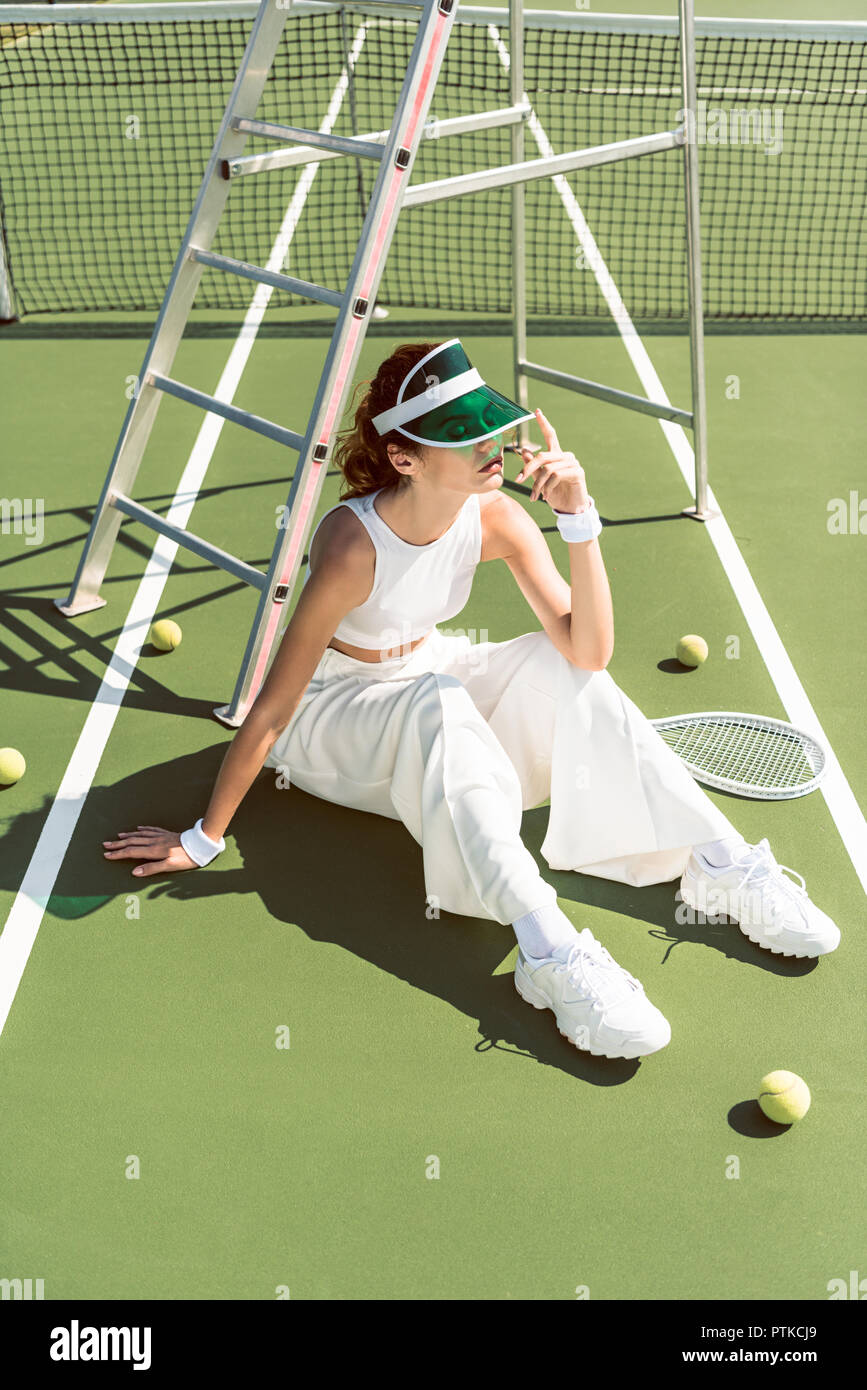 Giovane donna in moda abbigliamento bianco e cappuccio seduti sul campo da  tennis con racchette e palle Foto stock - Alamy