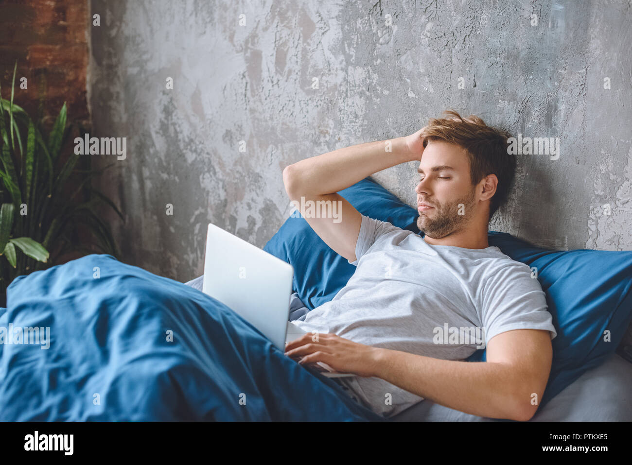 Sconvolto giovane uomo utilizzando laptop nel letto di casa Foto Stock