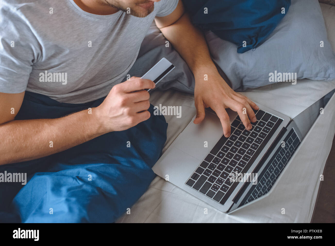 Immagine ritagliata dell uomo nel letto con carta di credito facendo shopping online su laptop Foto Stock
