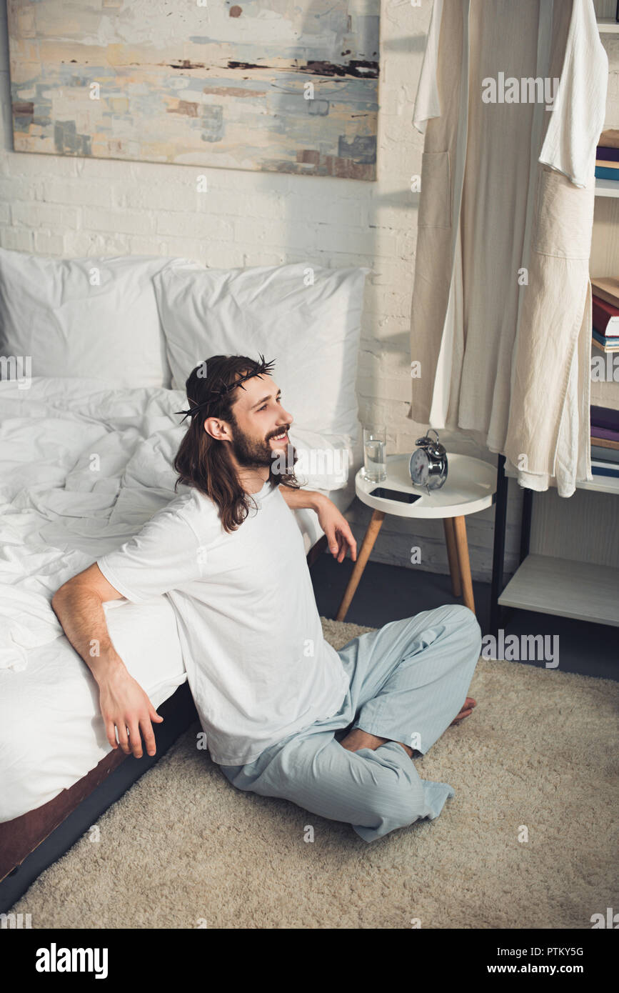 Alta vista angolare di sorridere Gesù seduto sul pavimento vicino al letto  durante la mattina tempo in camera da letto a casa Foto stock - Alamy