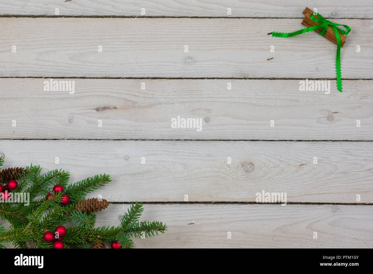 Abete rami nell'angolo inferiore sinistro con rosso grappoli di bacche e abete pigne lungo con bastoncini di cannella legati insieme con nastro verde in Foto Stock