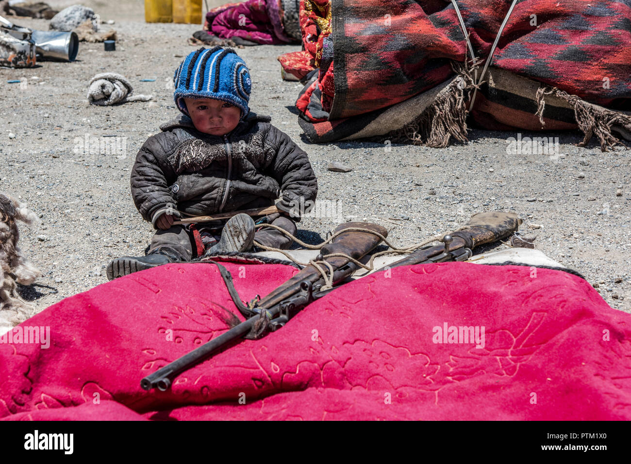 Un bambino del Kirghizistan guarda dopo fucili antichi mentre la famiglia imposta il loro accampamento nel Wakhan corridoio dell'Afghanistan. Foto Stock