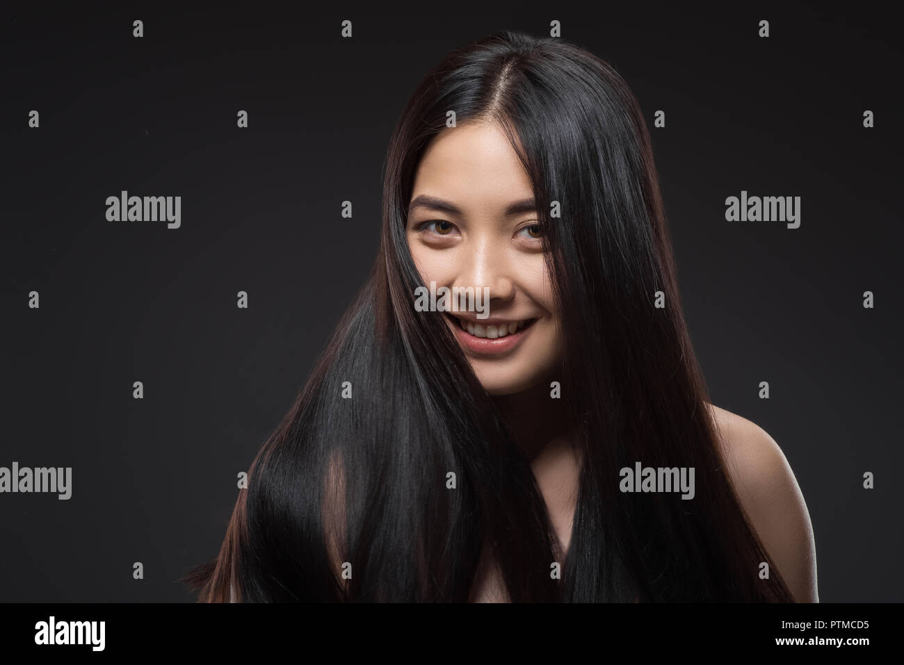 Ritratto di giovane sorridente donna asiatica con bella e sana capelli scuri guardando la telecamera isolato su nero Foto Stock