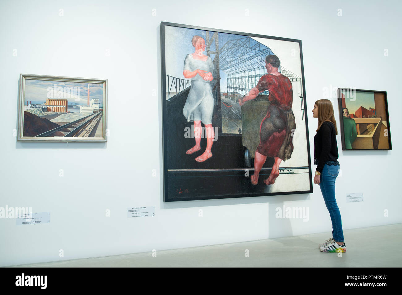 Il 10 ottobre 2018, Baden-Wuerttemberg, Mannheim: nella mostra "costruzione del mondo. Kunst und Ökonomie' nella Kunsthalle di Mannheim una foto dell'artista Alexander Deineka con il titolo "Beim Bau neuer Werkhallen' dal 1926. Sulla sinistra è il lavoro "classico paesaggio" (1931) da Charles Sheeler, sulla destra il 'Industriebild" (1924) di Karl Völker. Dalla giustapposizione di due epoche, la mostra espone per la prima volta la drammatica influenza di economia sull'arte. Foto: Uwe Anspach/dpa Foto Stock