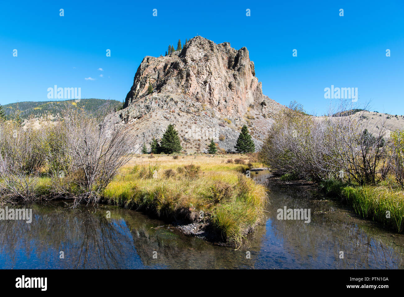 Robusta formazione di roccia, prato erboso e calma corrente di avvolgimento con riflessioni sotto un cielo blu brillante - Comanche punto nel New Mexico settentrionale Foto Stock