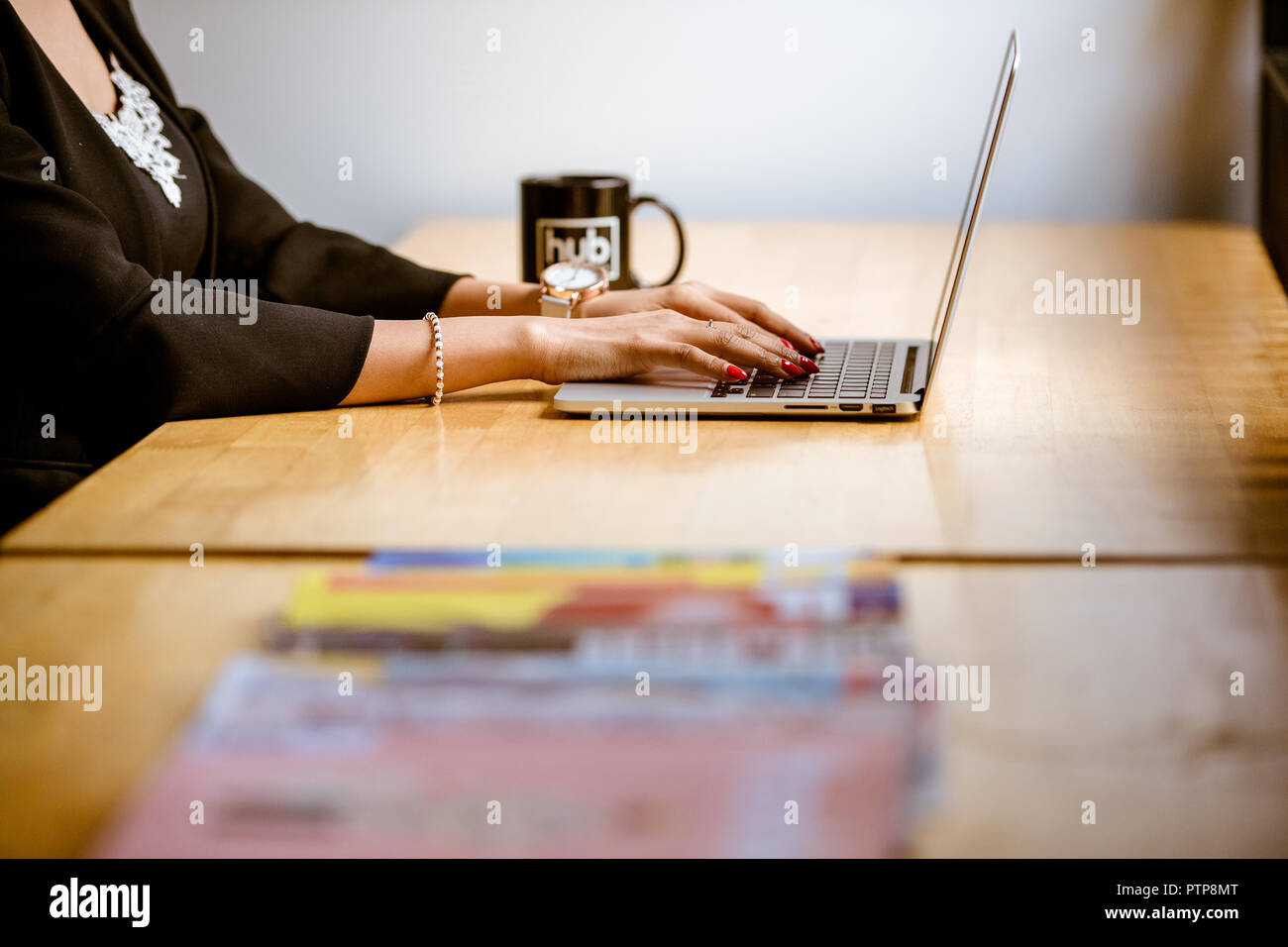 Primo piano delle braccia di una donna che digita su un computer portatile in ufficio. Foto Stock