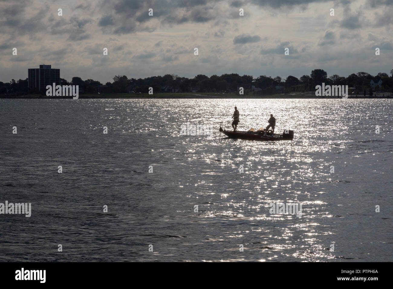 Detroit, Michigan - due uomini la pesca da una piccola barca sul Fiume Detroit. Windsor, Ontario, Canada si trova sul lato più lontano. Foto Stock