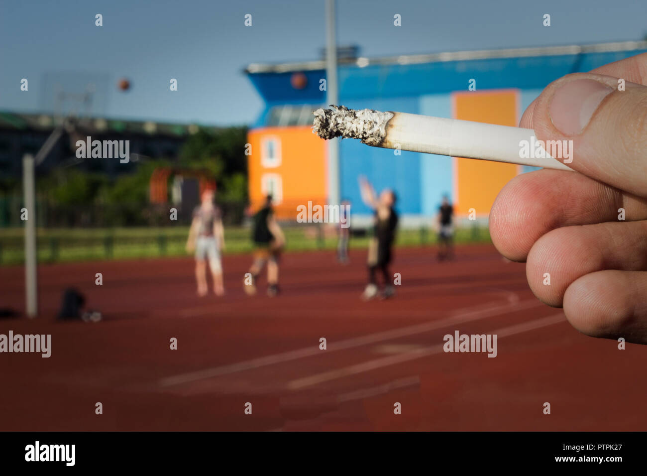 Un uomo tiene una sigaretta in background dello stadio in cui giocare a basket, close-up, cattiva abitudine Foto Stock