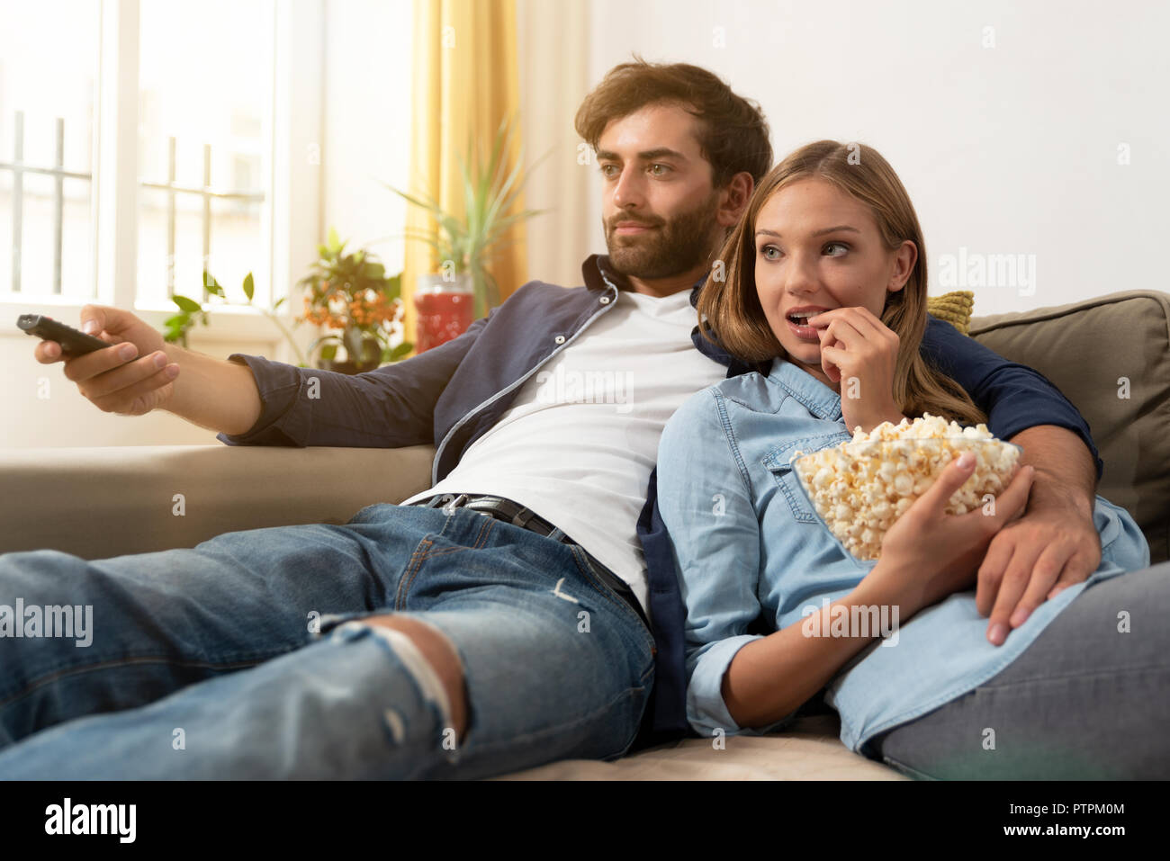 Giovane guardando la TV, mangiare popcorn su un divano a casa Foto Stock