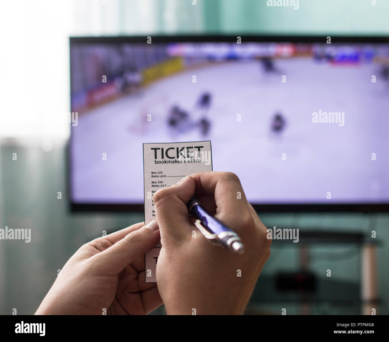 Un uomo detiene un bookmaker ticket e scommesse sportive, in TV va di hockey, close-up Foto Stock