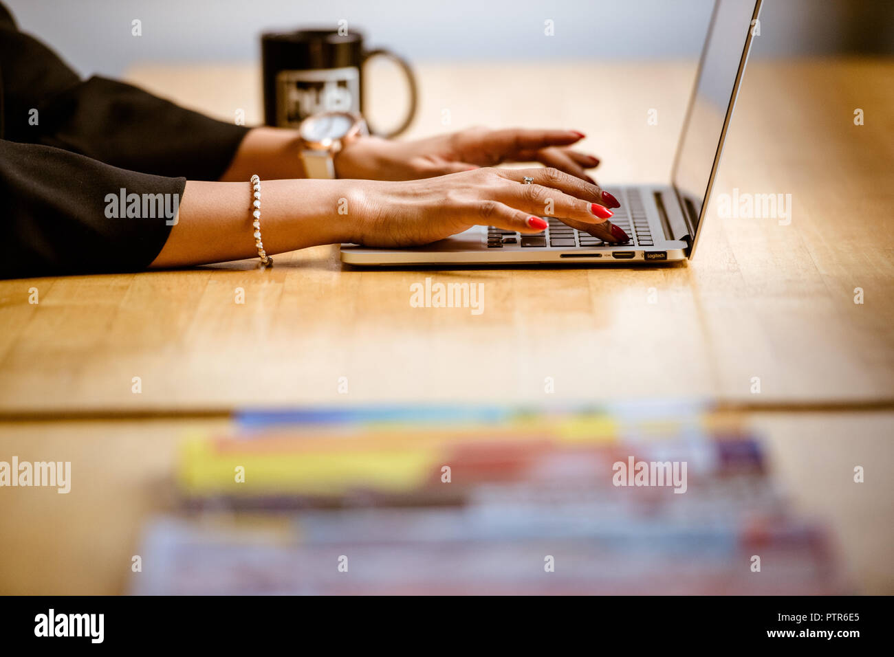 Primo piano delle braccia di una donna che digita su un computer portatile in ufficio. Foto Stock