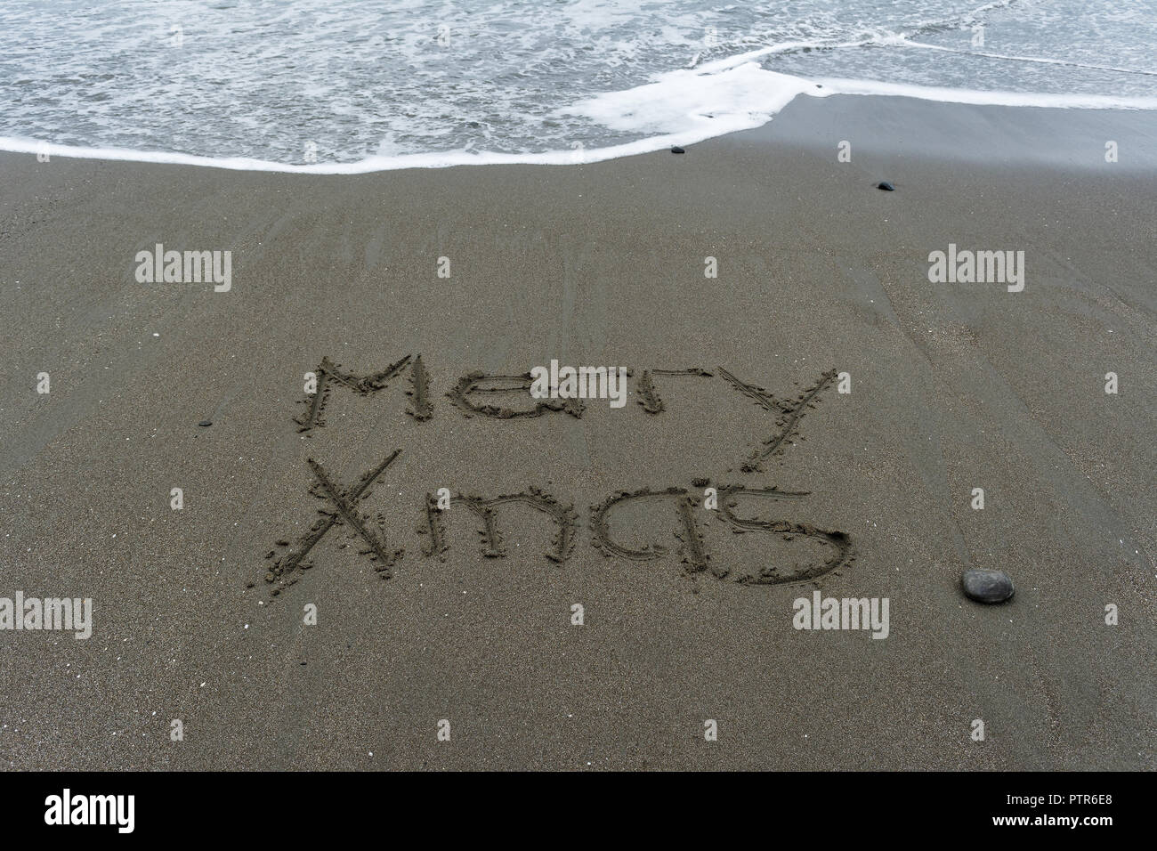 Un'onda giri verso Merry Xmas scritto nella sabbia Foto Stock