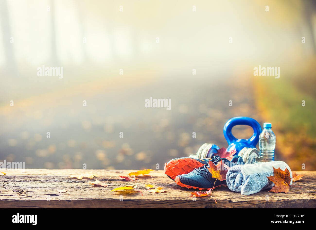 Coppia di blu scarpe di sport di acqua e manubri prevista su una tavola di legno in un albero autunno alley con foglie di acero - accessori per eseguire l'esercizio o worko Foto Stock