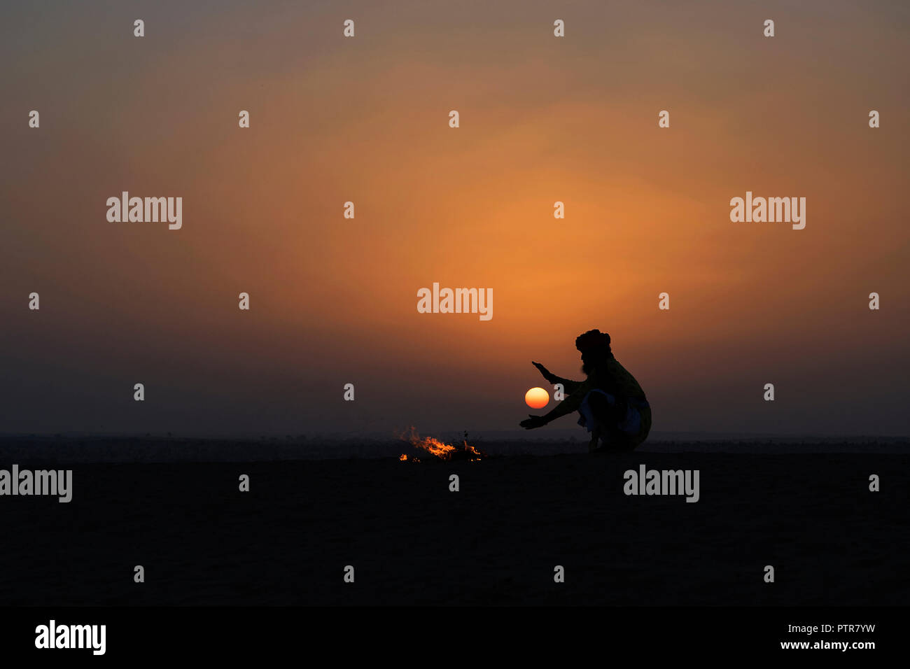 Rajasthani uomo tradizionale riscaldando le mani sul fuoco in dune di sabbia. Foto Stock