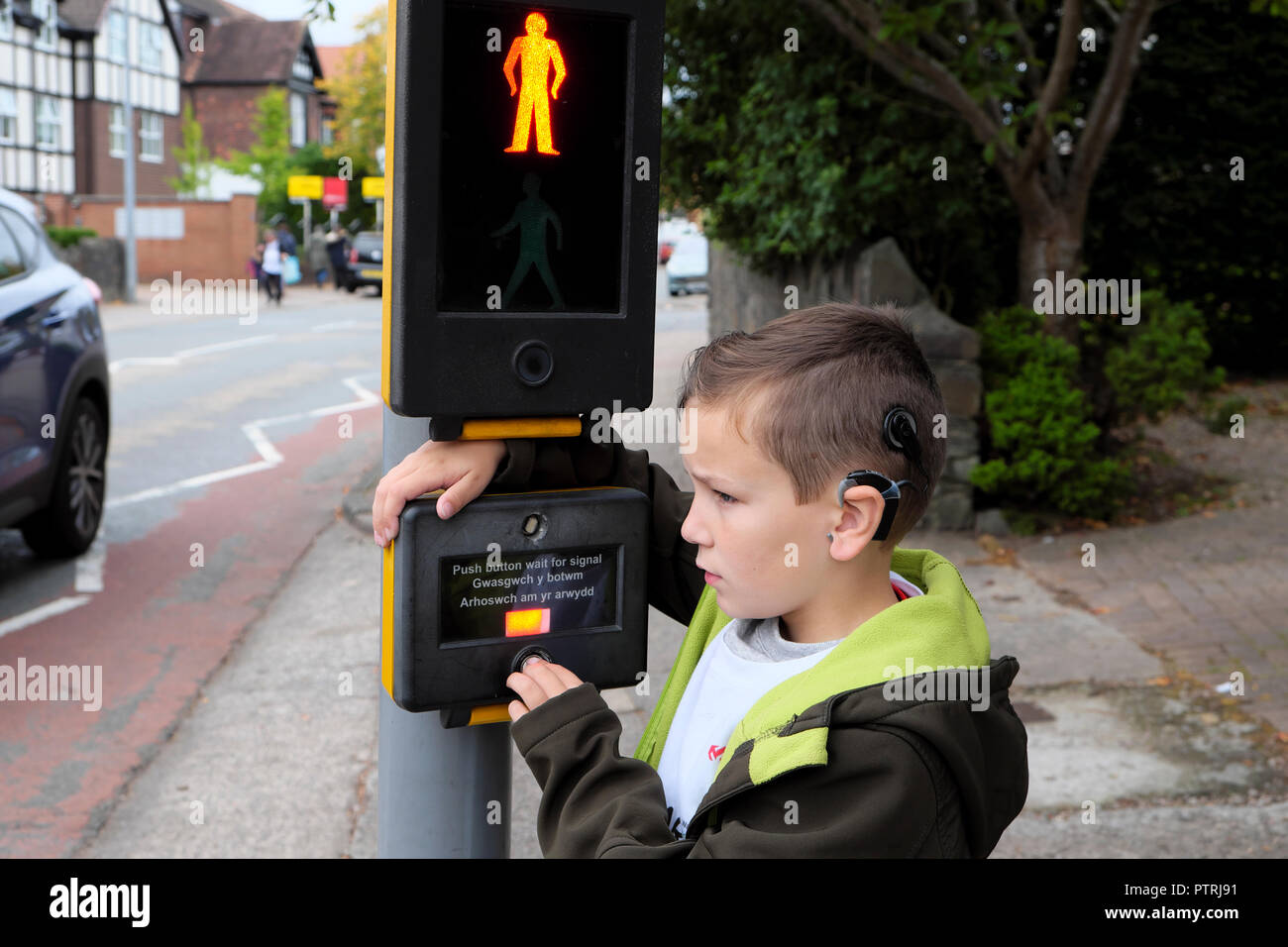 Un ragazzo giovane 8 andare a scuola a piedi in attesa di attraversare la strada ad un traffico pedonale luci segno di incrocio in una zona urbana UK KATHY DEWITT Foto Stock