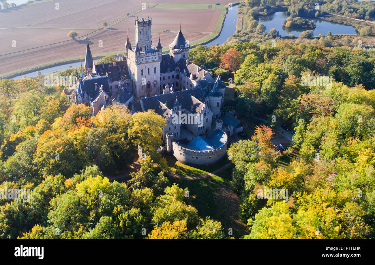 Pattensen, Bassa Sassonia. Undicesimo oct, 2018. Il Castello di Marienburg si erge nella luce del sole di mattina in mezzo autunnali alberi scoloriti (fotografia aerea con drone). Re Giorgio V di Hannover ha avuto il neo-gotico residence costruito tra il 1858 e il 1869. 150 anni più tardi il castello è di proprietà privata da Ernst August principe di Hannover Jr e una popolare meta escursionistica nella regione di Hannover. Credito: Julian Stratenschulte/dpa/Alamy Live News Foto Stock