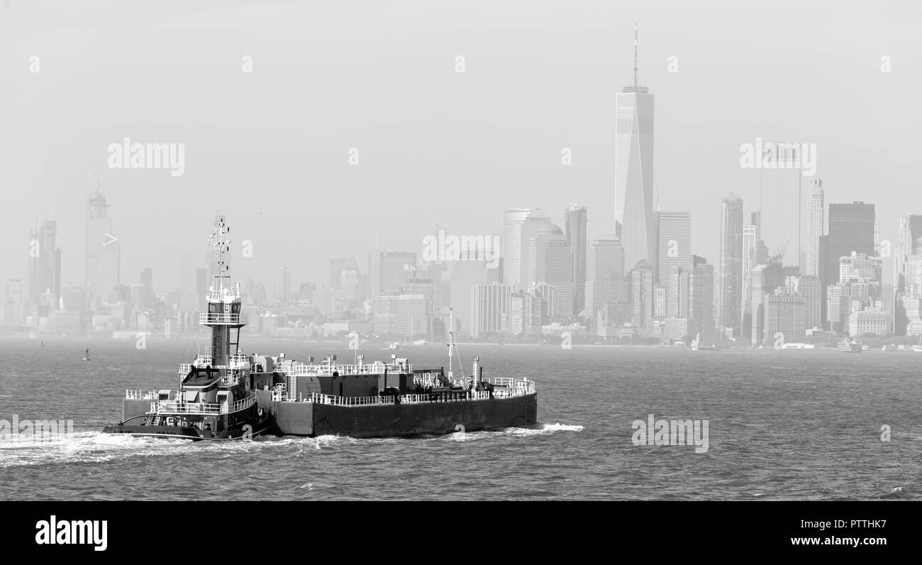 Freight tug spingendo nave da carico per il porto di New York City e la parte inferiore di Manhattan skyscarpers skyline in background. Foto Stock