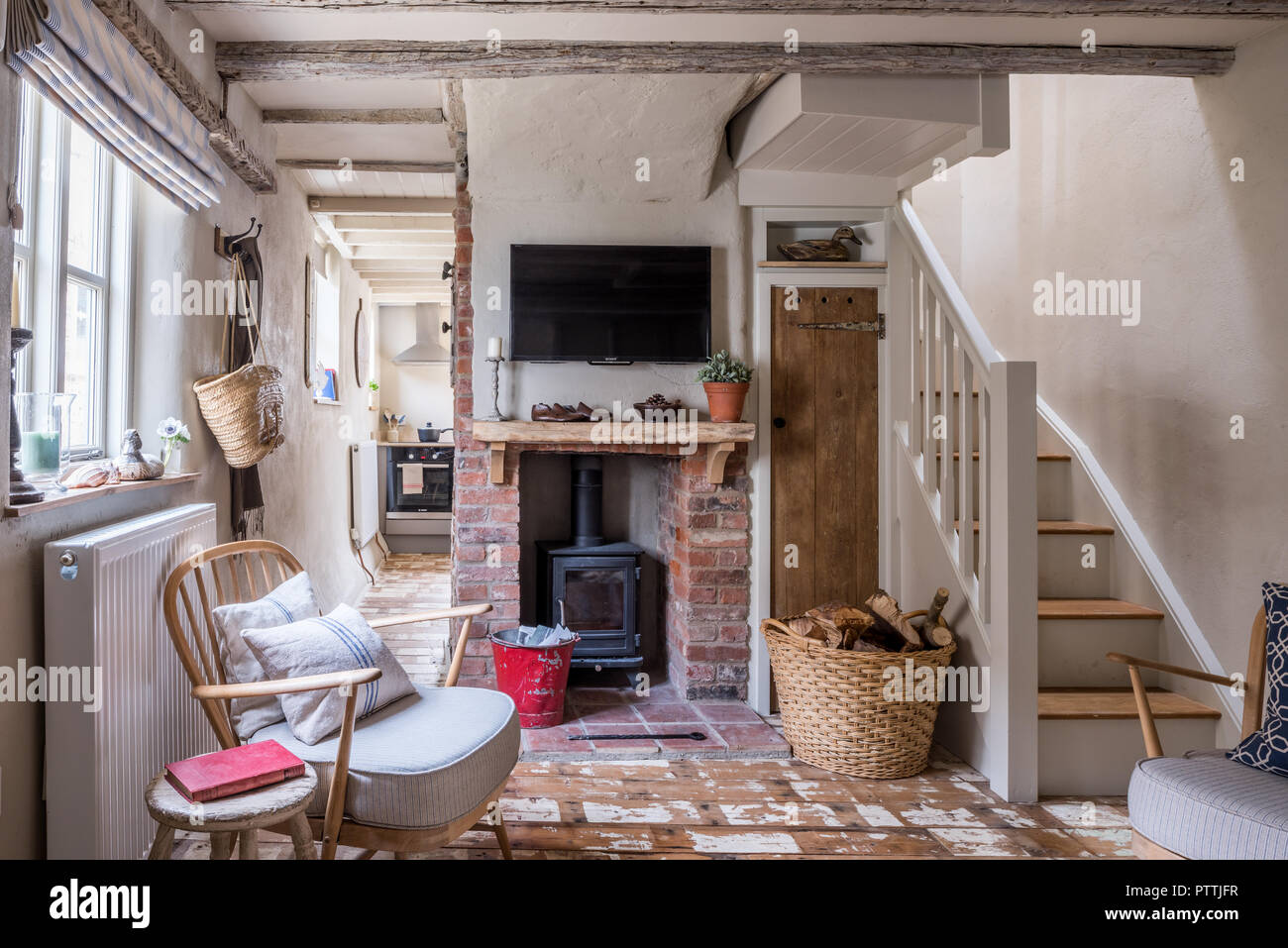 Stripped Ercol-style poltrona e montato a parete TV sopra esposti caminetto in mattoni con woodburner Foto Stock