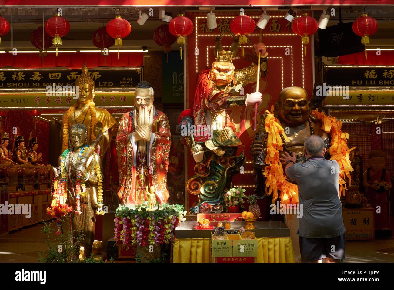 Per raggiungere una buona fortuna, un adoratore accarezza il ventre di una Hotei o ridere statua del Buddha in un santuario Taoista a Waterloo Street, l'area di Bugis, Singapore Foto Stock