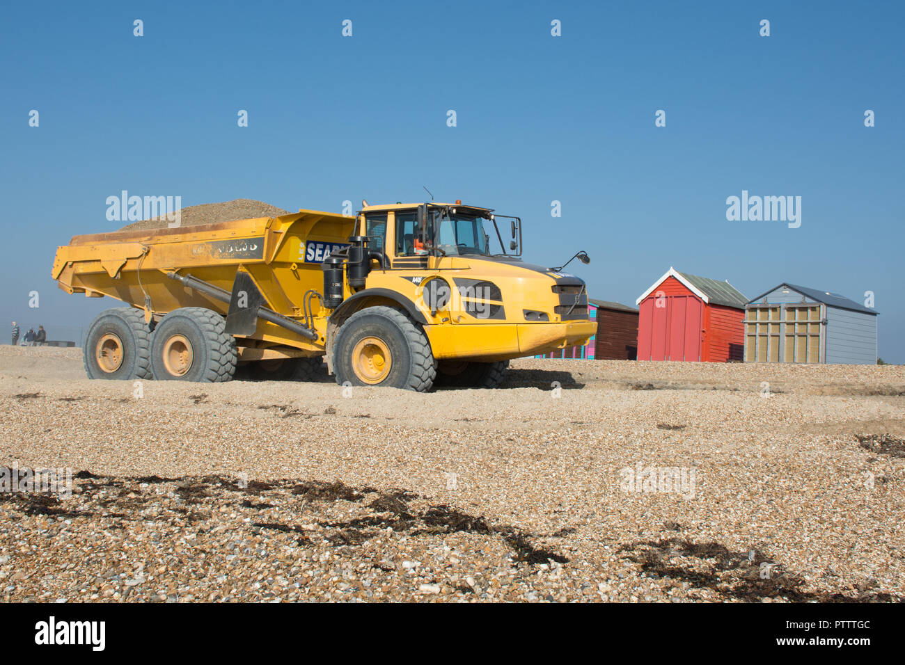 Giallo carrello ribaltabile sulla spiaggia a Hayling Island lo spostamento o il trasporto di un carico di ghiaia per migliorare le difese costiere Foto Stock