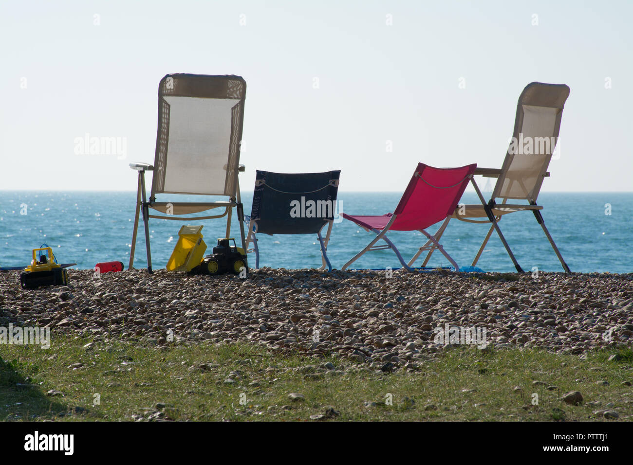 Vuoto quattro sedie pieghevoli su una spiaggia di ciottoli in riva al mare Foto Stock