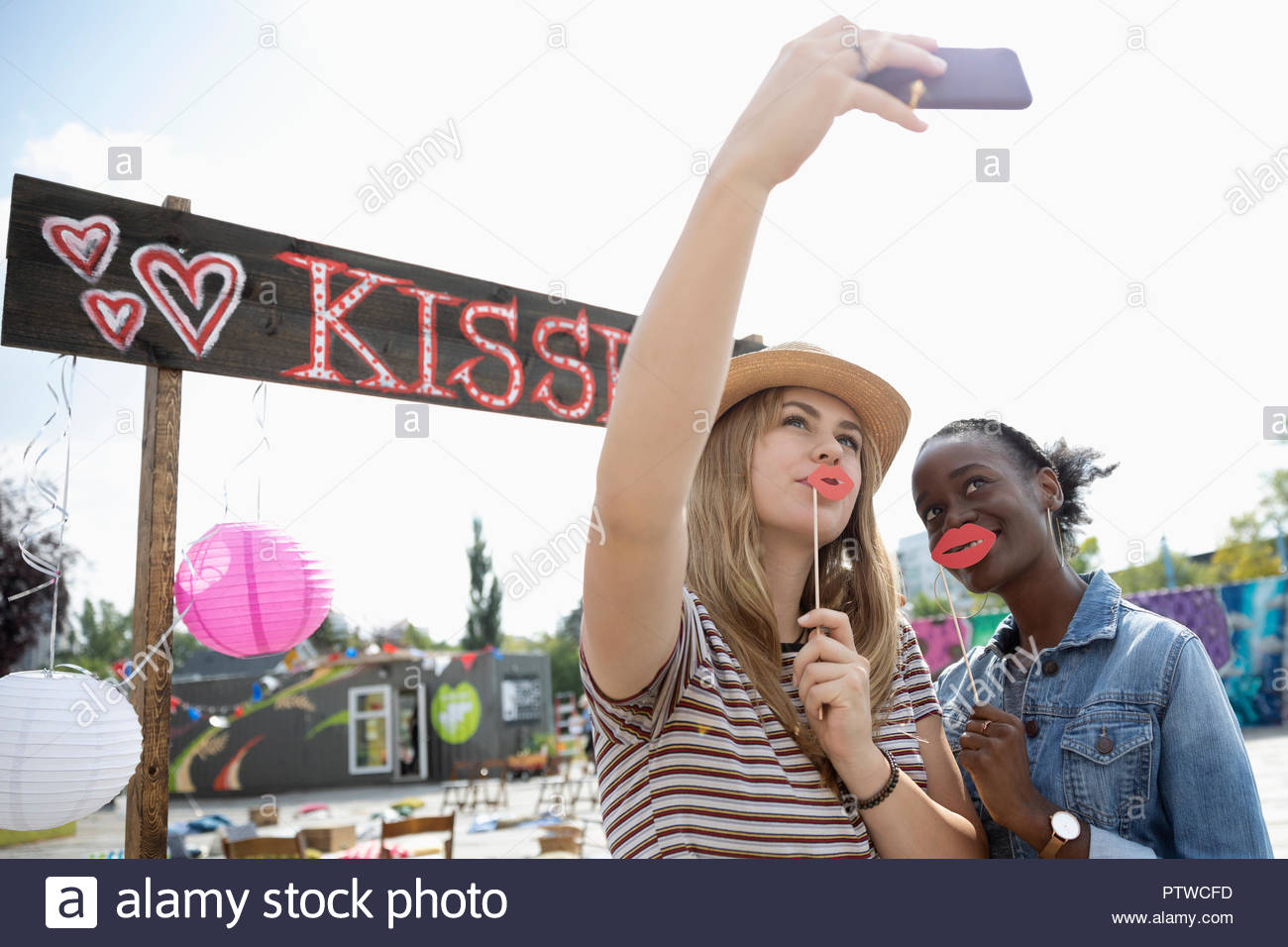 Giocoso giovani donne con labbro colonnette tenendo selfie a baciare booth Foto Stock