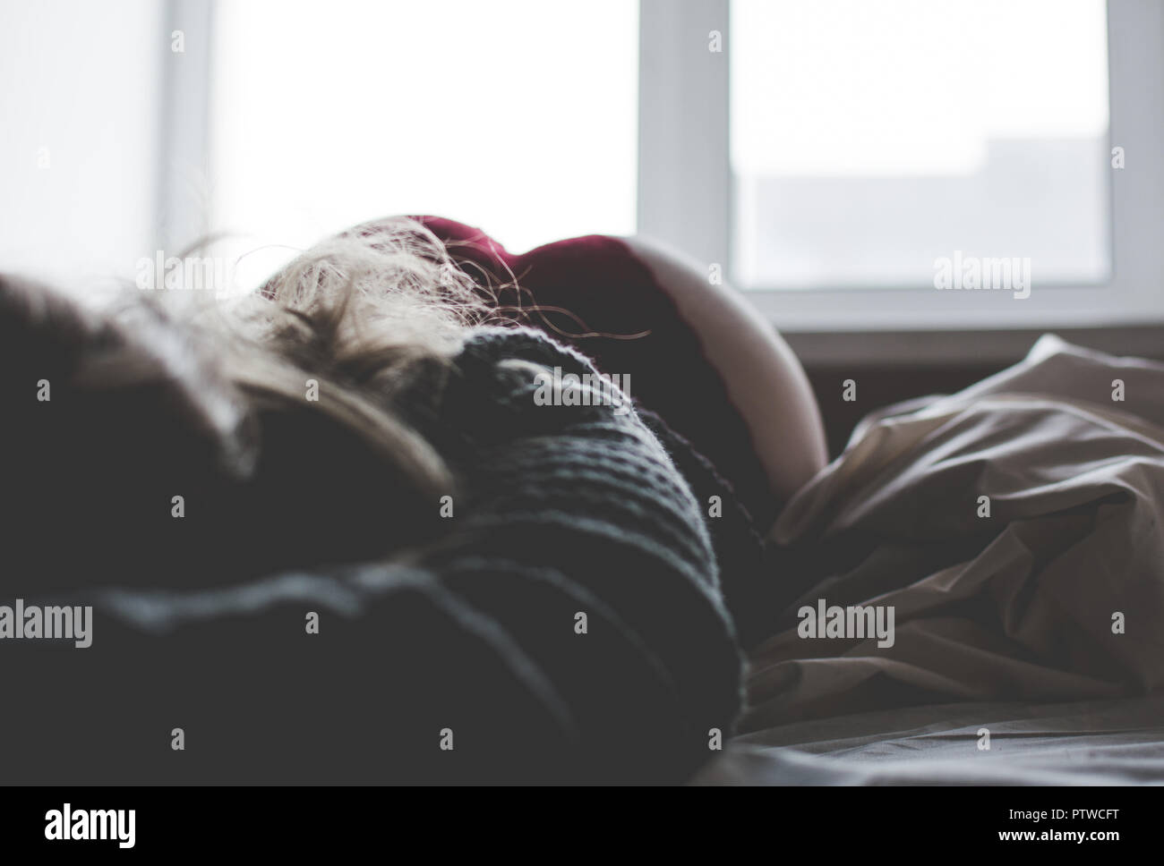 Bella ragazza in maglione grigio su un letto bianco Foto Stock