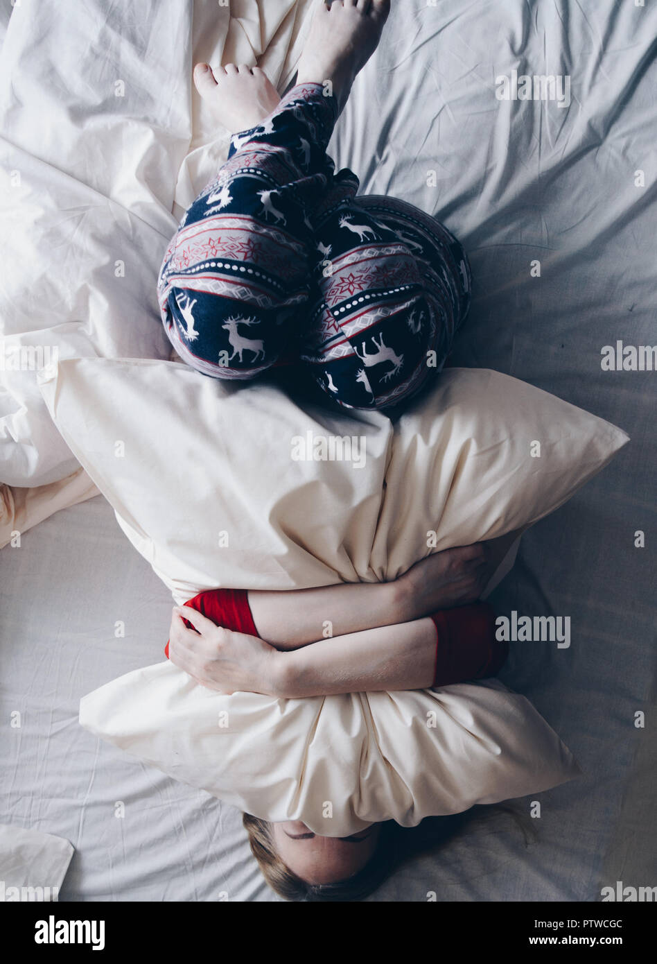 Felice ragazza in inverno abiti sul letto bianco abbracciando un cuscino. Foto Stock