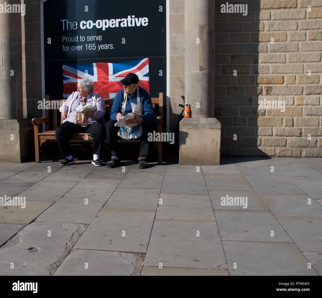 Una coppia di anziani di sedersi su un sedile al di fuori del negozio cooperativo in Bakewell, Derbyshire mangiare pesce e patatine. Foto Stock