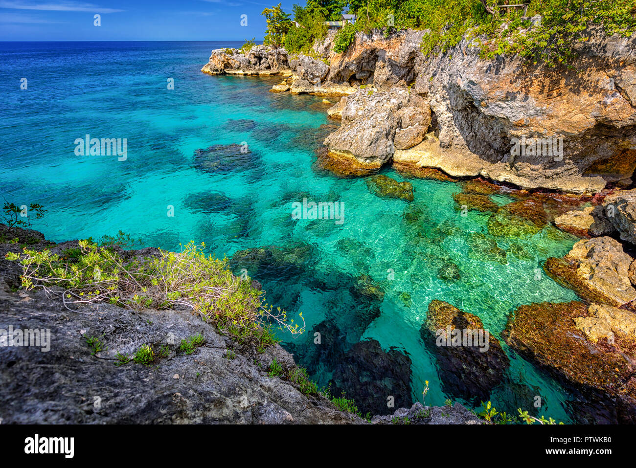 Bella turchesi acque cristalline in prossimità di rocce e dirupi in Negril. Caribbean Paradise Island e acqua al mare con un cielo blu Foto Stock