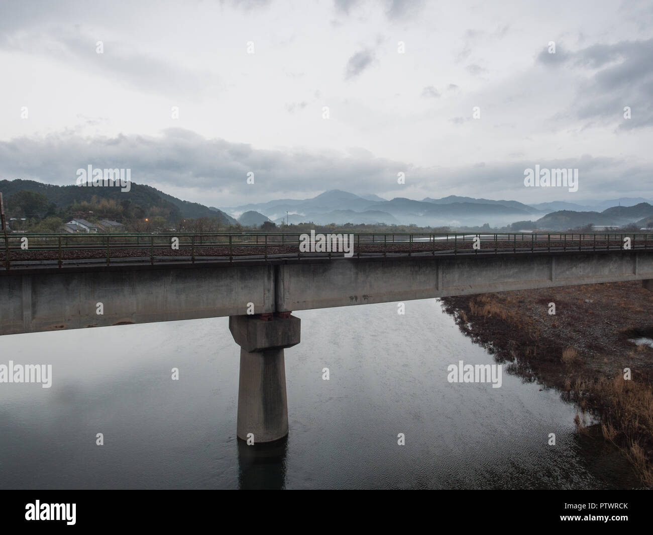 Ponte ferroviario sulla Kaifu River, guardando a monte, grigio cielo cloud e nebbioso hils Tokushima, Giappone Foto Stock