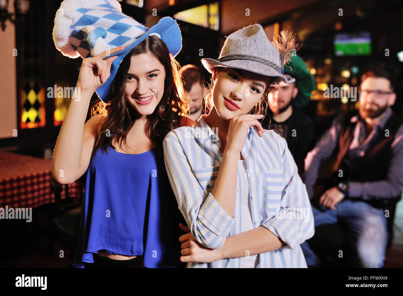 Due simpatici giovani fidanzate in cappelli bavarese sorridente al bar di fondo durante la celebrazione dell'Oktoberfest Foto Stock