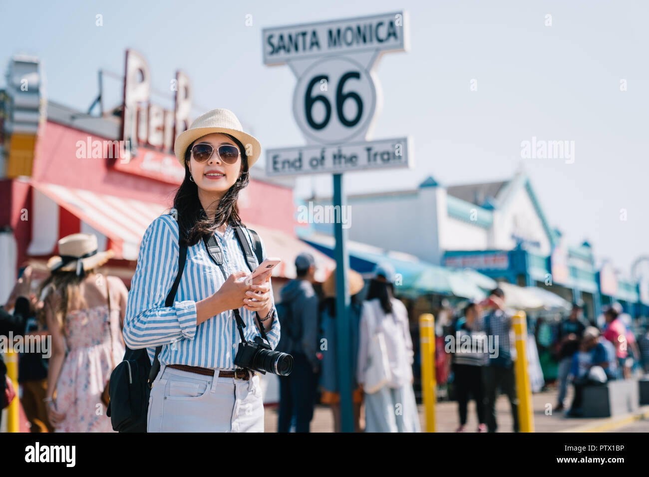 Un elegante turista femminile tramite cellulare di controllo della mappa, in piedi accanto al segno di Santa Monica Foto Stock